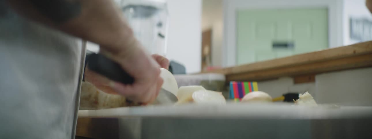 A tattooed man in a kitchen cutting a yellow onion
