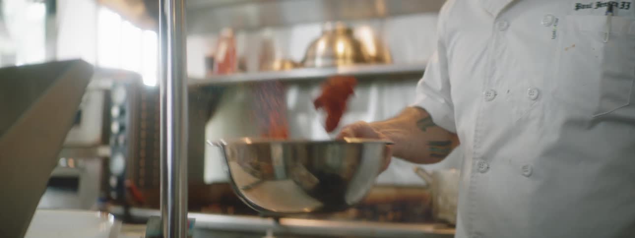 A chef mixing spices in a bowl in a kitchen