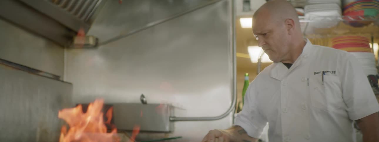 A chef shaking a flaming skillet on a stovetop