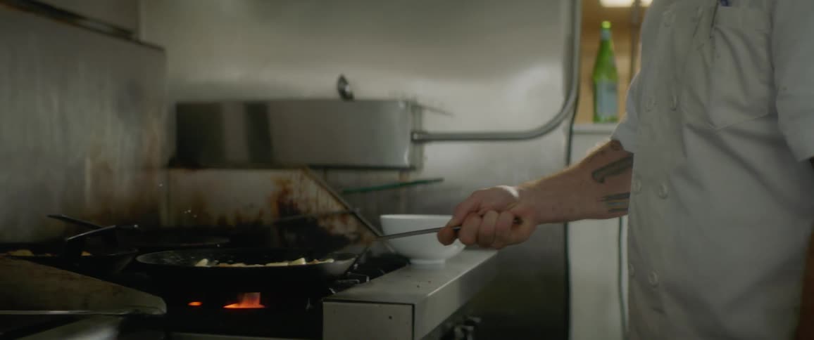 A man cooking food in a pan under a flaming burner