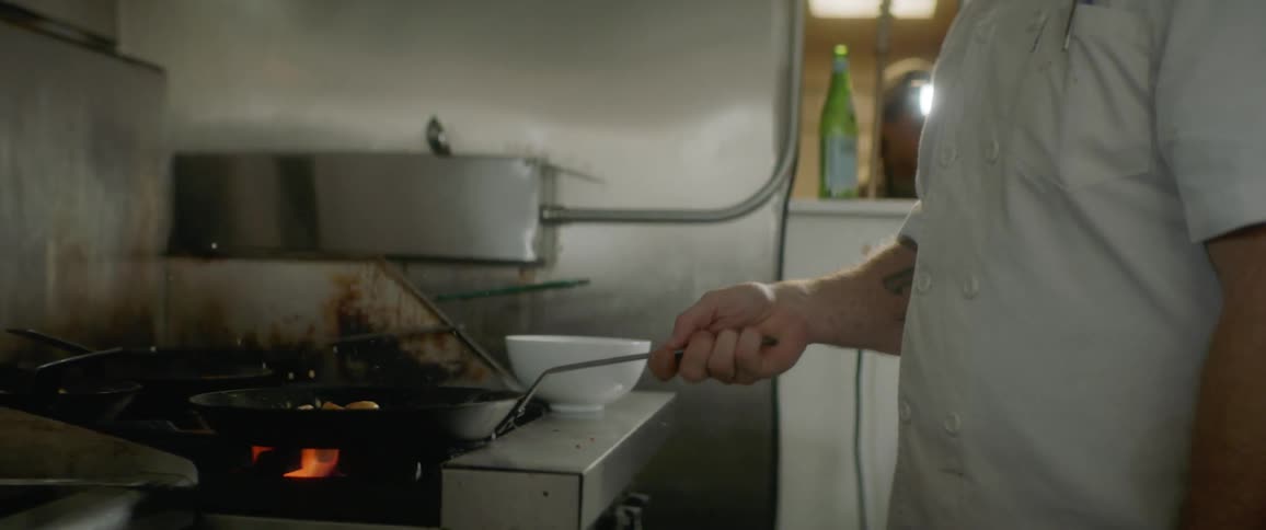 Man flips meat in pan over gas burner in commercial kitchen