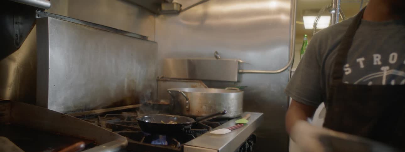 A cook puts a pan on the stove and begins cooking ingredients