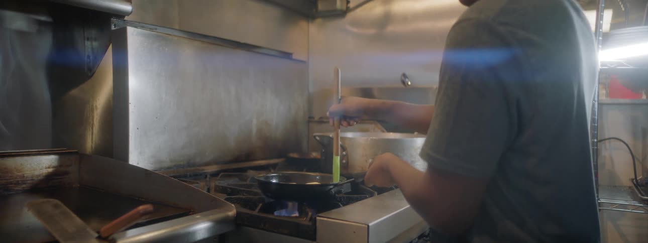 A man is cooking with a pan at the stove