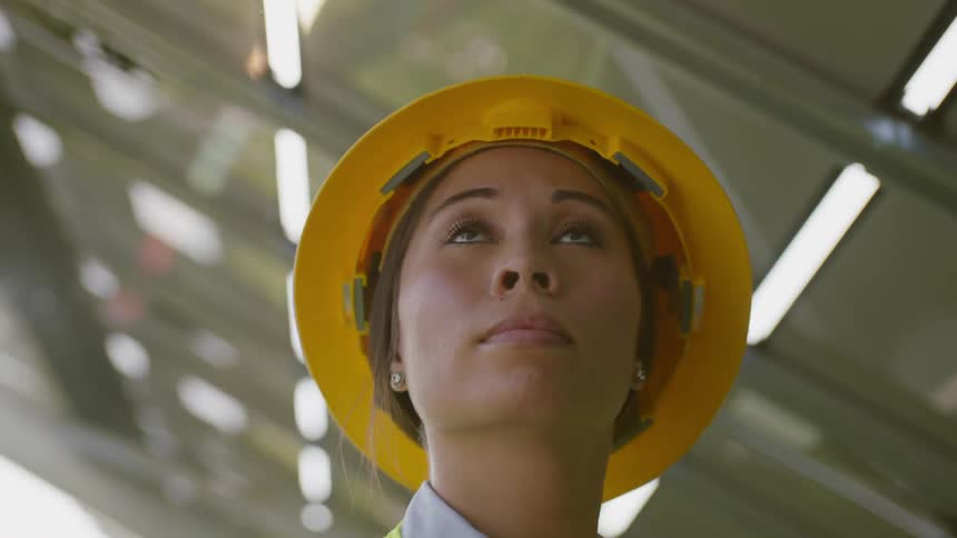 A woman is looking around wearing a hard hat