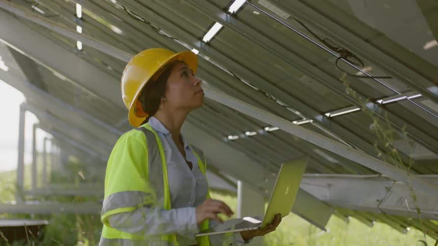 A black construction worker types on a laptop and inspects a structure