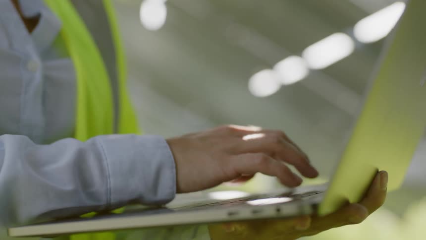 Woman wearing helmet holds laptop and types on it during the day