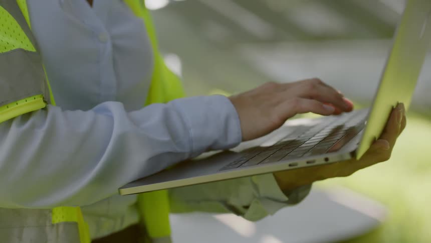 Woman types on laptop she is holding in one hand