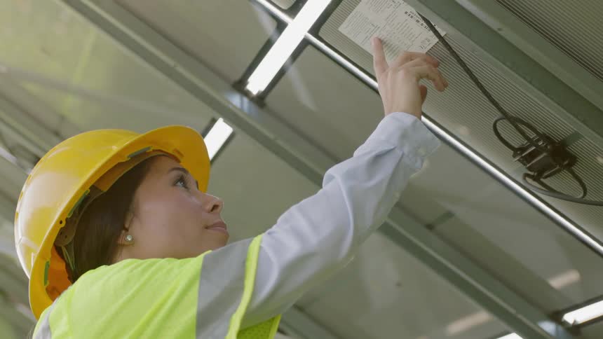 A female in a yellow hard hat looks overhead at a checklist posted above her