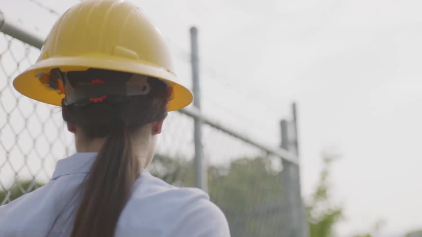 Woman in a hard hat opening a chain link fence and walking through