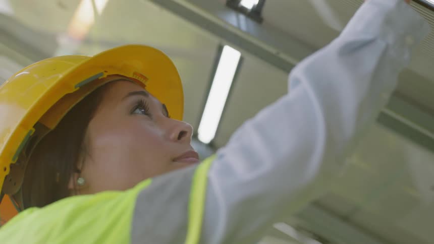 Female worker wearing hard hat points at instructions on the ceiling