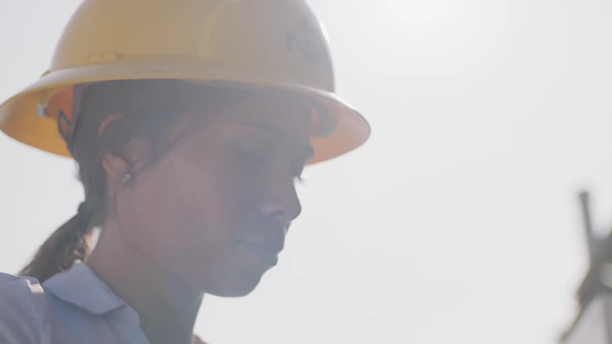 Woman in hard hat typing on laptop outdoors