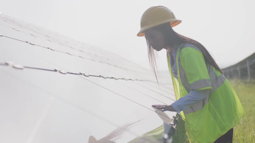 A black woman in a hard hat and reflective vest examining a structure