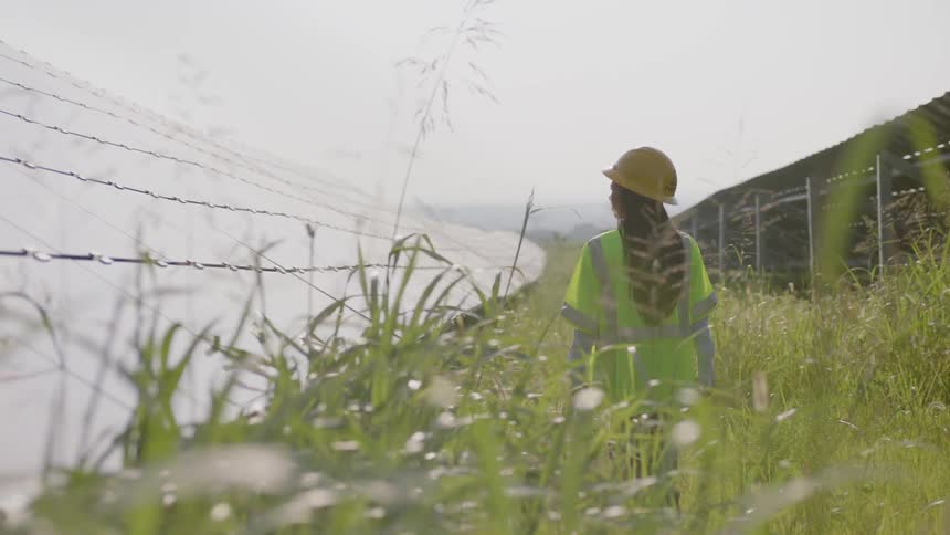 A woman wearing a helmet and high visibility clothing walks a perimeter