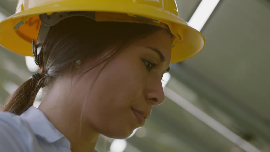 A woman wearing a hard hat is typing one handed on a laptop