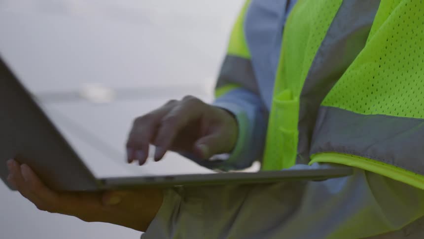 Woman in a green visibility vest and hard hat works on a laptop