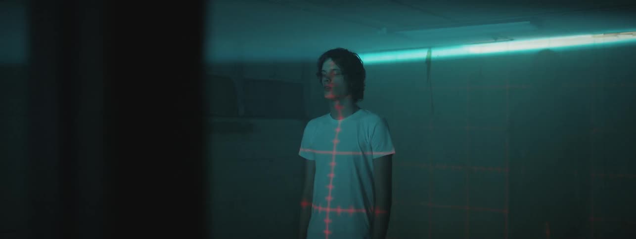 A young white man stands in a dark room and is scanned with lasers