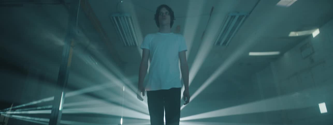 A man walks towards the camera with lights flashing behind him