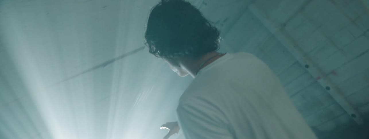 A young white man stands in a dark room pointing his arm straight forward