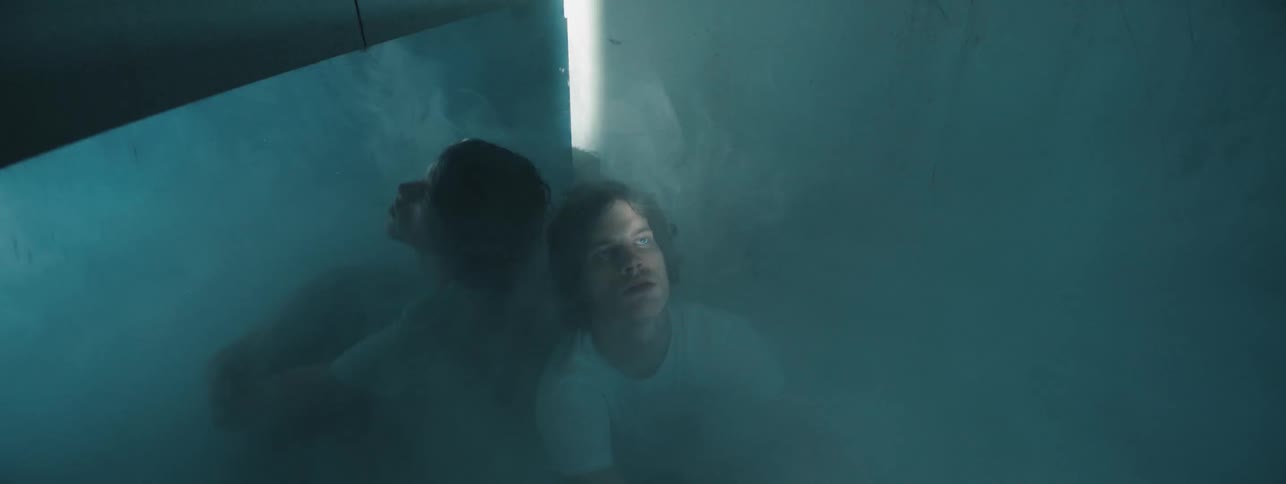 A man sits in the corner of a dark foggy room