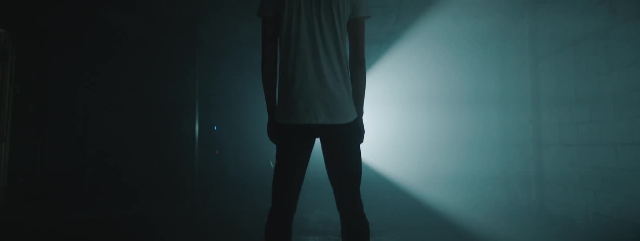 A beam of light repeatedly passes over a teenage boy standing in a dark room