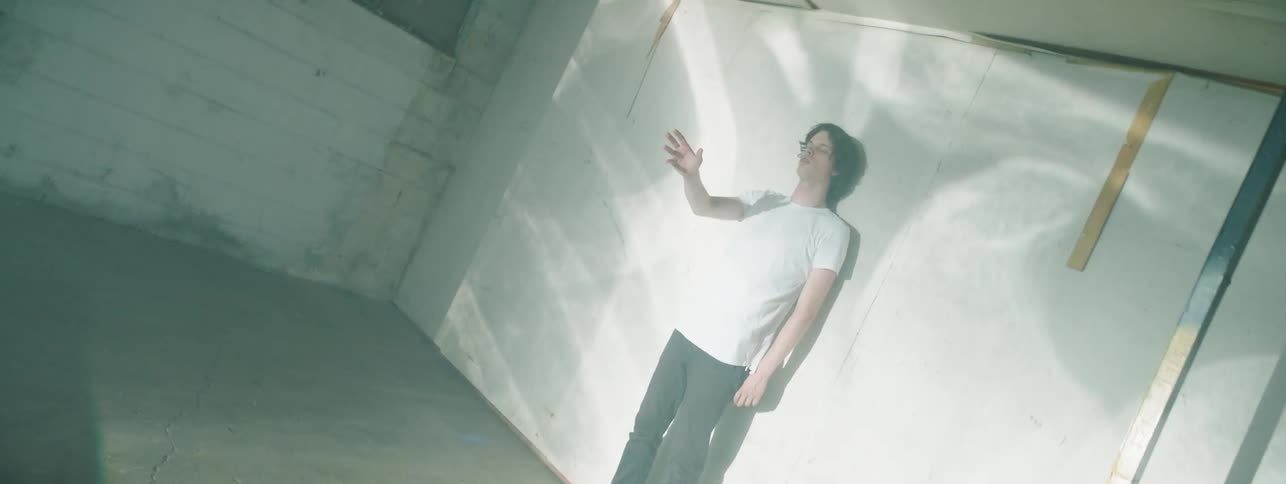 A young man stands in an empty room against the wall as a series of abstract images and images of medical x rays are projected onto him and the wall behind him in a very rapid manner