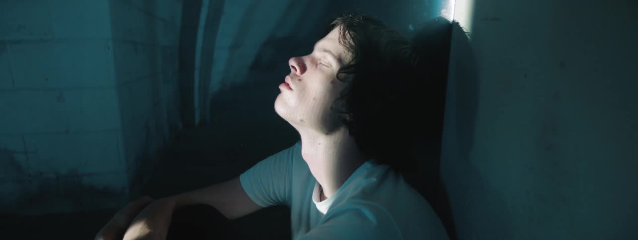 A man sits on the floor with his head against the wall