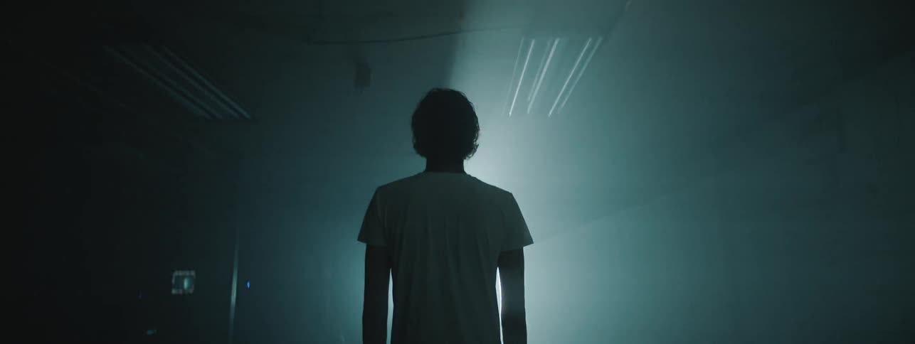 A strobe light circles a man who is standing in a darkened room
