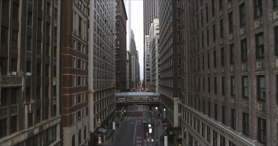A downtown city street which runs between high rise buildings of both modern and period architecture