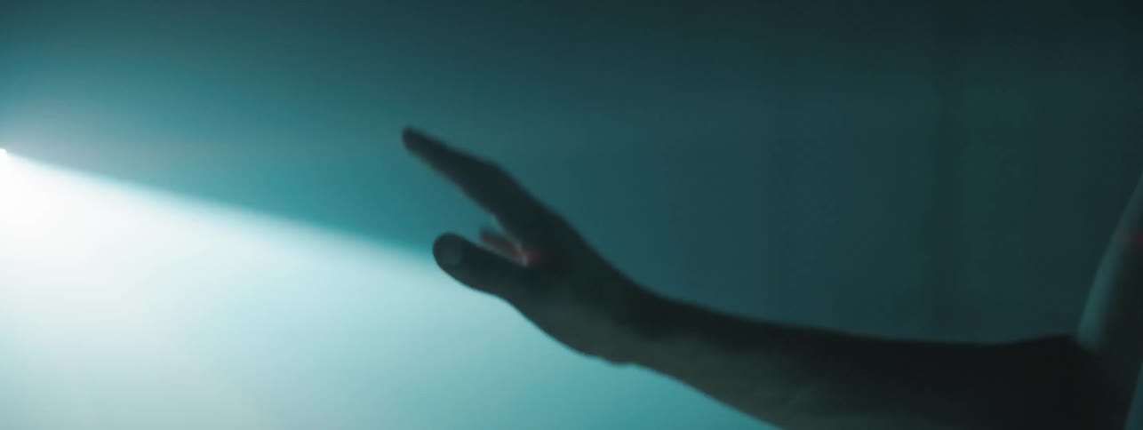 The hand of a young man is seen with a bright flashing light projected onto it while hes in a dark room