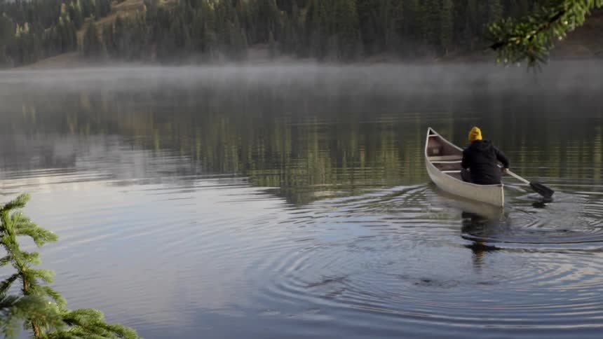 Person paddles their canoe into misty water
