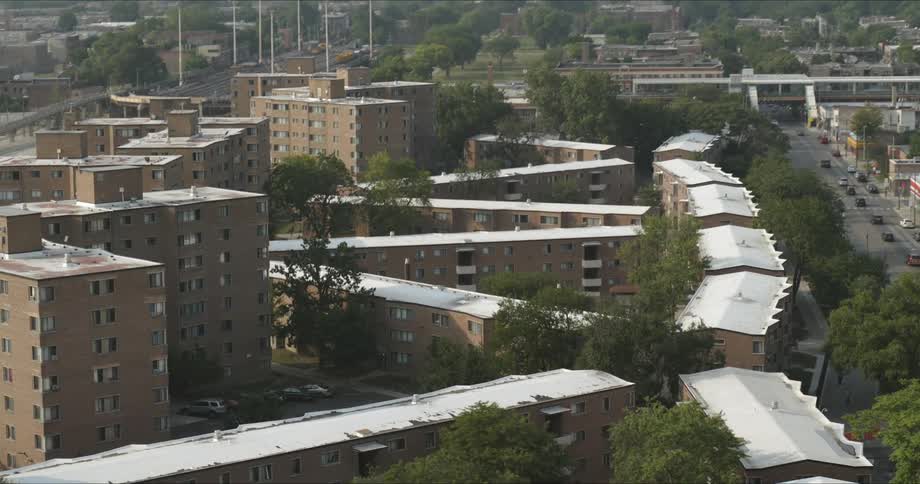 Rooftops of apartment buildings and row houses in an urban neighborhood with a city skyline on the horizon
