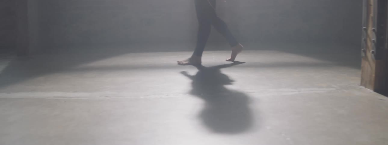A person walks across a bare floor casting a shadow