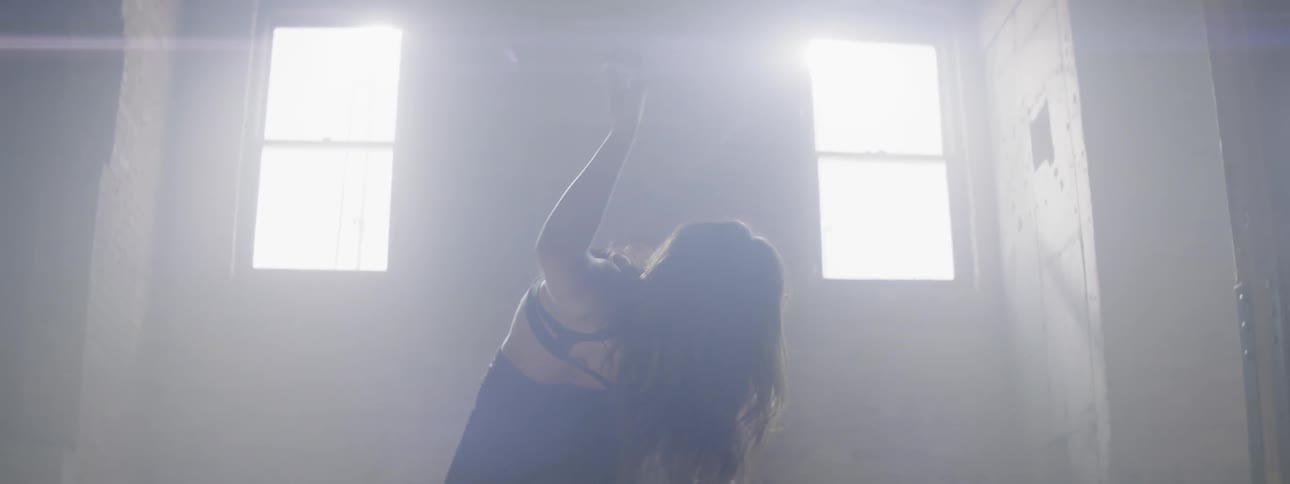 A woman dances in front of bright windows
