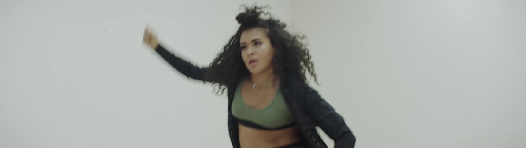 Curly hair girl wearing sports bra dances between four white walls