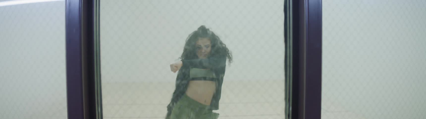 Woman performing dance moves behind a glass panel