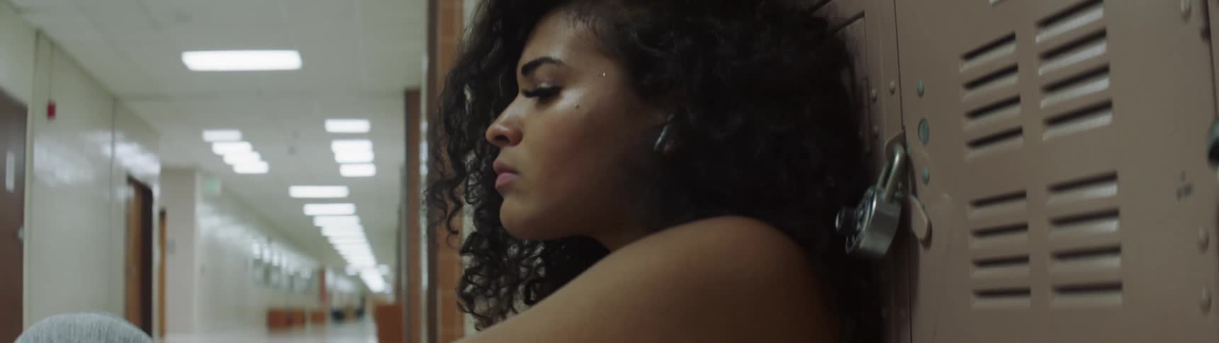 A young black girl sits against a locker