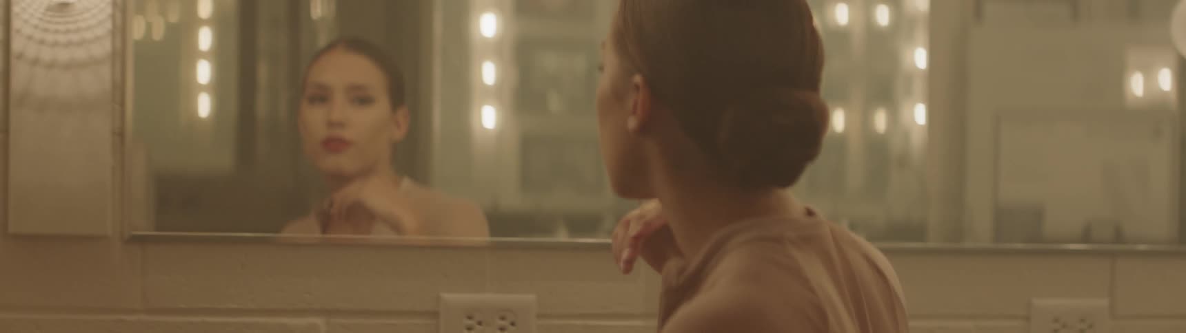 Woman turns to look at herself in lighted vanity mirror