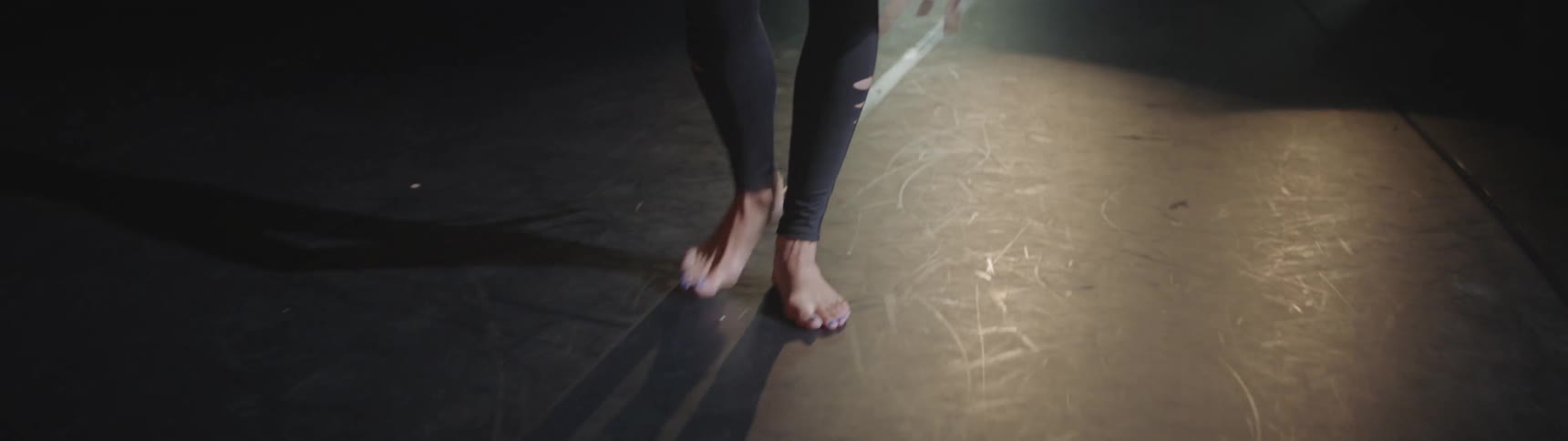 A dancer walks across a stage carrying ballet slippers
