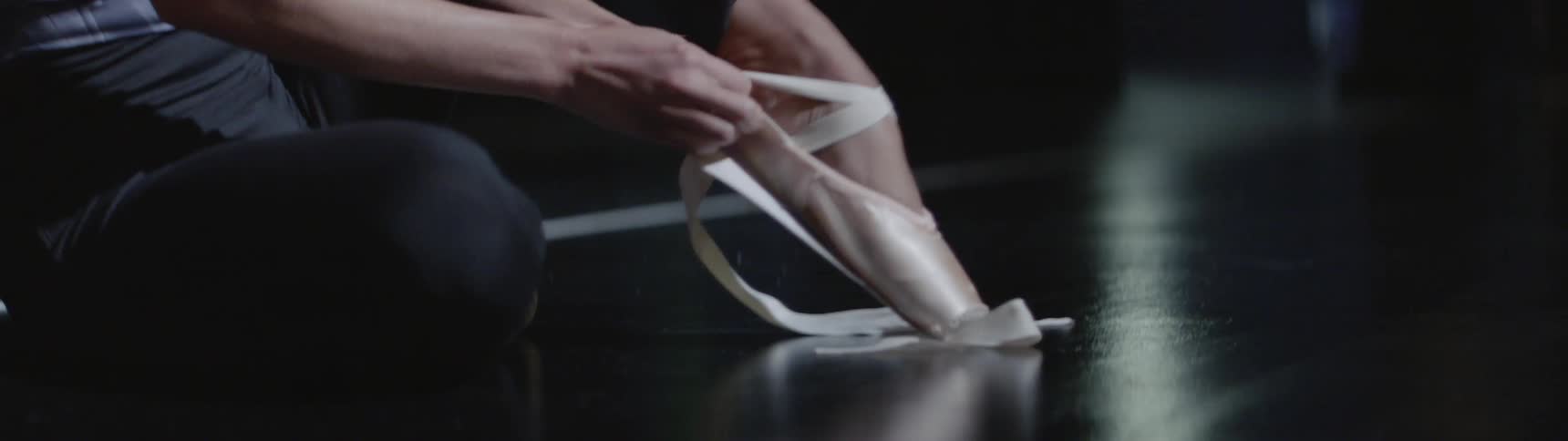 A ballet dancer puts on her shoes and stretches