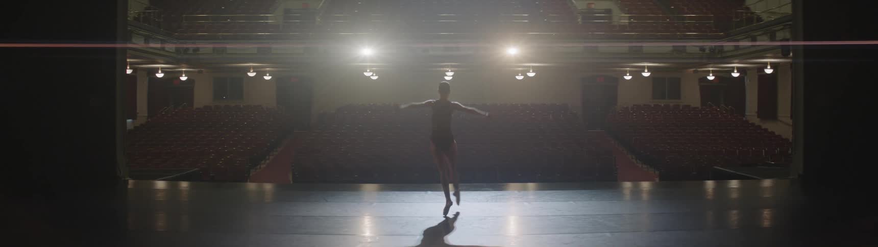 A ballerina performs on stage in an empty theater
