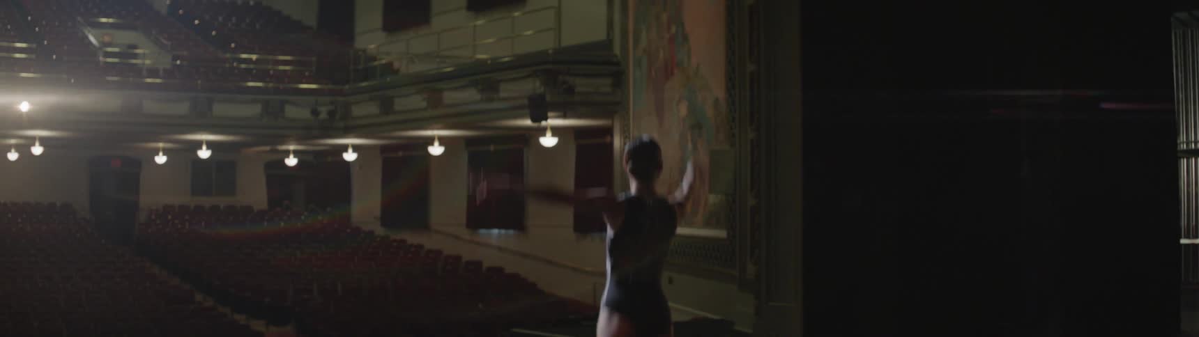 A woman practices ballet in an empty auditorium