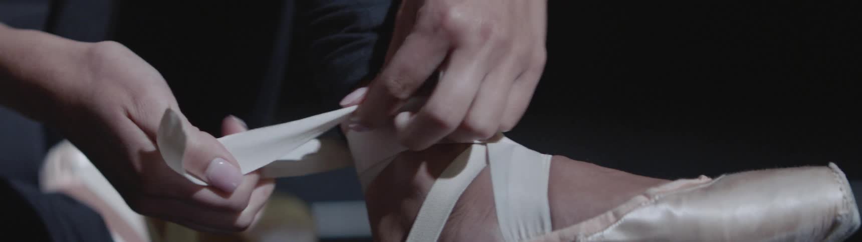 A ballerina ties her shoes to her ankle