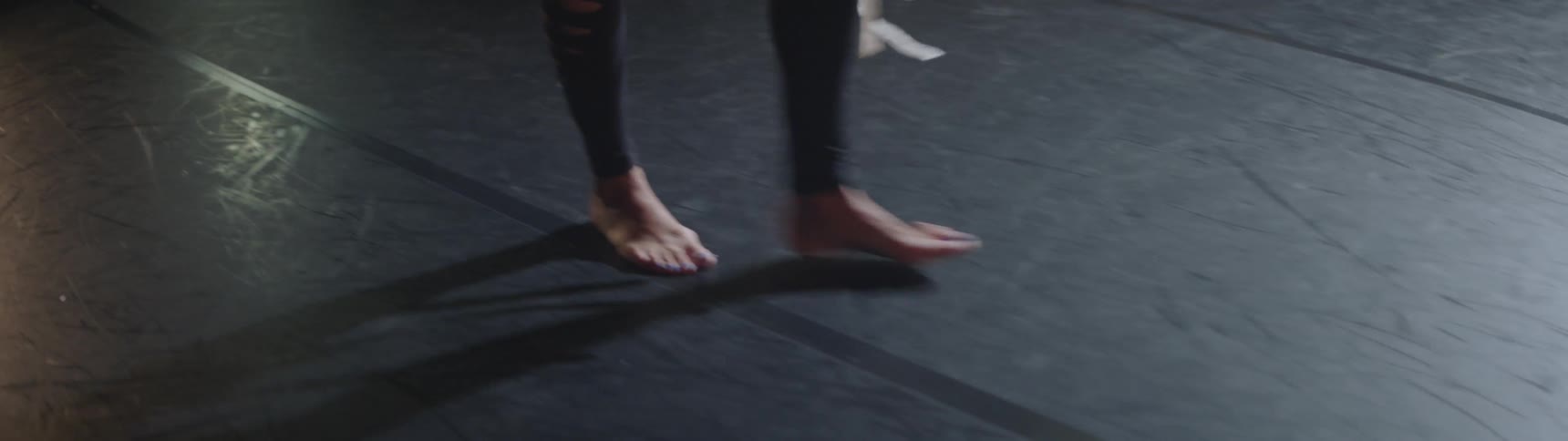 A ballet dance walks barefoot while holding her shoes
