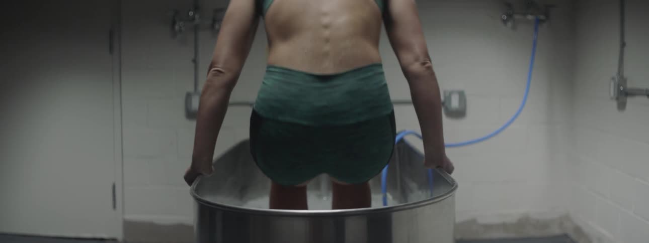 Woman on a sportswear enters a metal bathtub full of ice