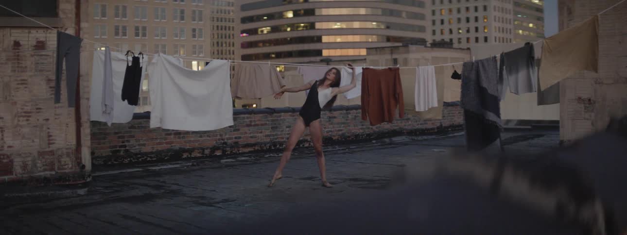 A woman dances on a rooftop in front of laundry drying on a clothesline