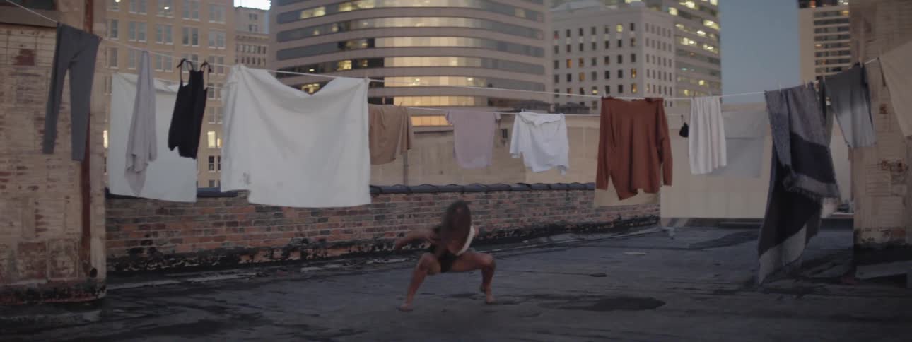 A woman dances near laundry on a clothesline in a city