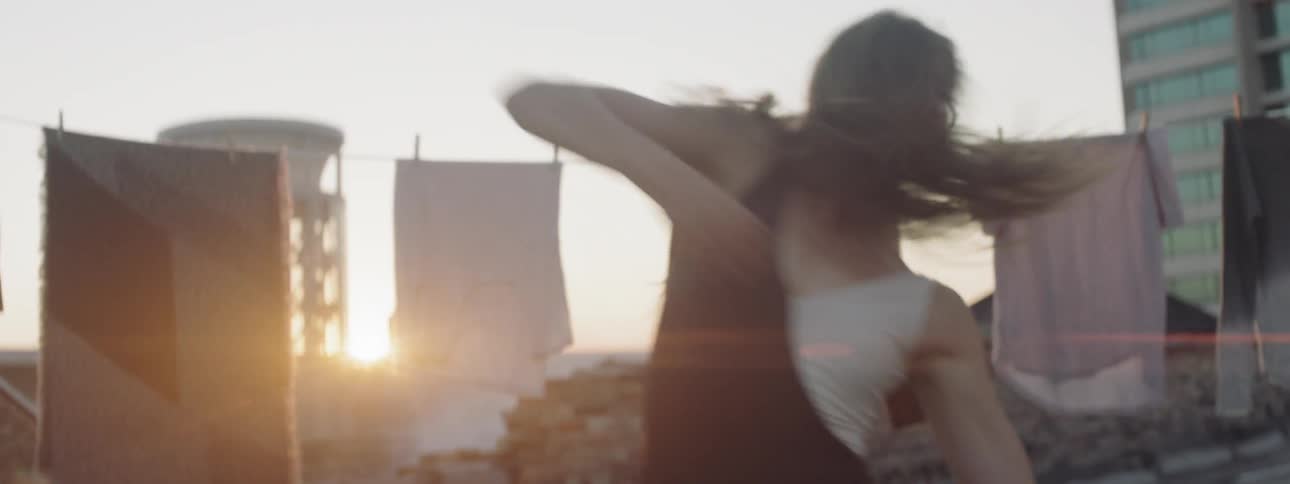 A woman does a dance in front of a clothesline on a city rooftop