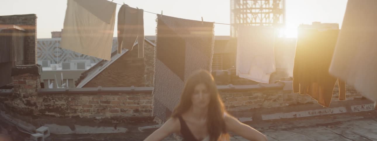 A woman dances on a rooftop surrounded by clothing hung on lines