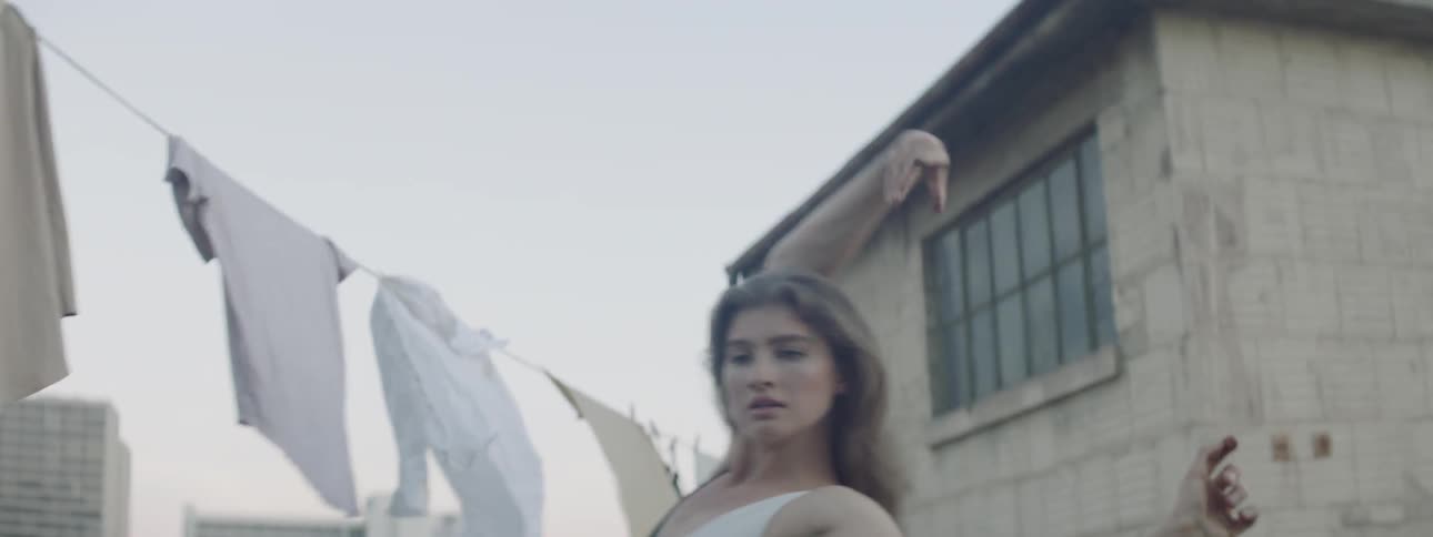 A white woman in a one piece bathing suit dances on a rooftop