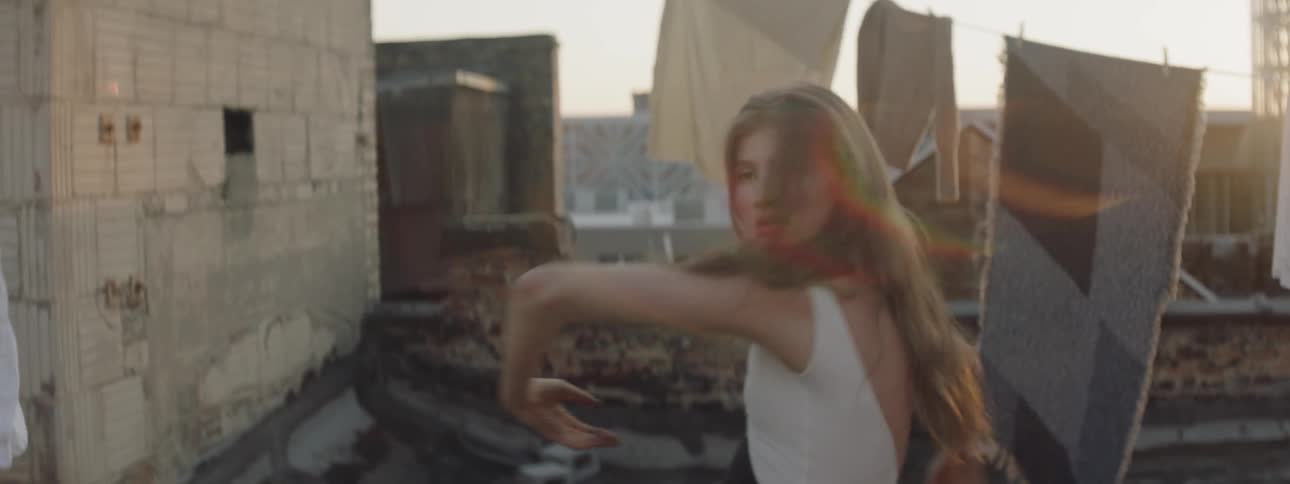 Woman in leotard dances on rooftop between lines of laundry at sunset